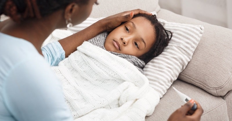 Mother presiding over sick daughter in bed, suffering from the flu and cough